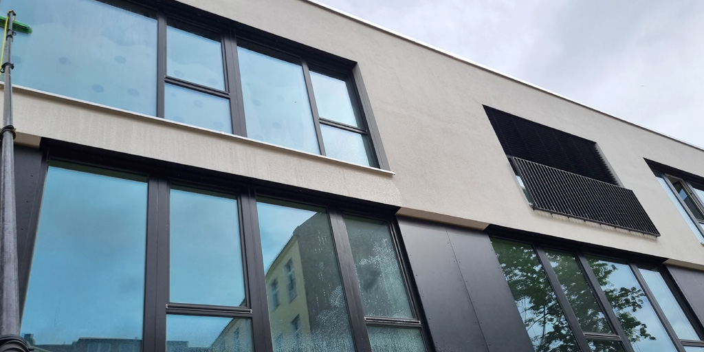 Fensterreinigung in Berlin zum Festpreis: Fassadenfenster werden mit eine Teleskopstange von außen geputzt